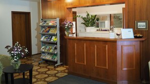 A reception desk with a wooden finish, a bookshelf with magazines, a vase with flowers, and a framed picture on the wall. - Waldhotel Porta Westfalica garni (Porta Westfalica)