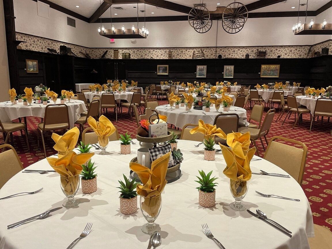 A banquet hall with round tables set for dining, each with a centerpiece of yellow napkins and small potted plants.
