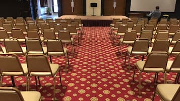 Un salón de conferencias con filas de sillas orientadas hacia una gran mesa y una pantalla de proyector.