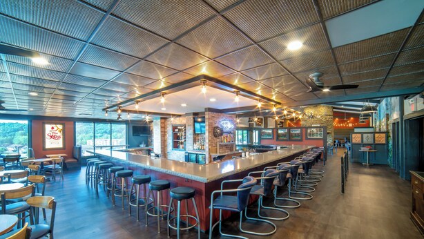 A spacious bar area with a long counter, multiple stools, and a high ceiling with exposed beams. - The Seasons Lodge (Nashville)