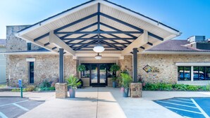 A building with a stone facade, a covered entrance with a geometric roof design, and a parking lot with marked spaces. - The Seasons Lodge (Nashville)