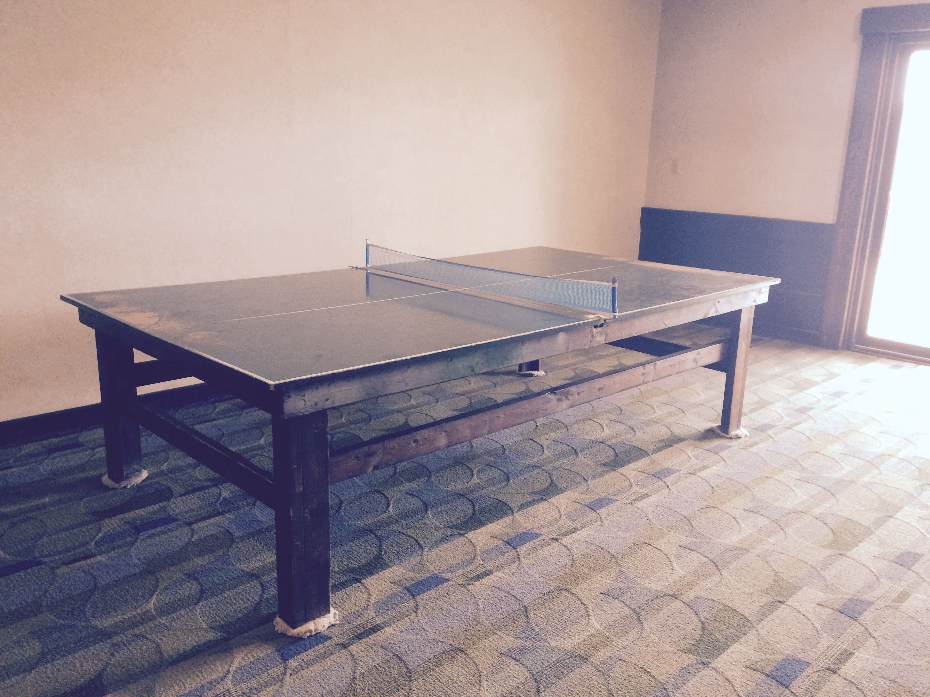 A ping pong table in a room with patterned carpet and a plain wall.