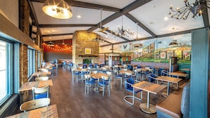 A spacious restaurant with high ceilings, exposed beams, and a mural depicting a scenic landscape. Tables and chairs are arranged in a casual layout. - The Seasons Lodge (Nashville)