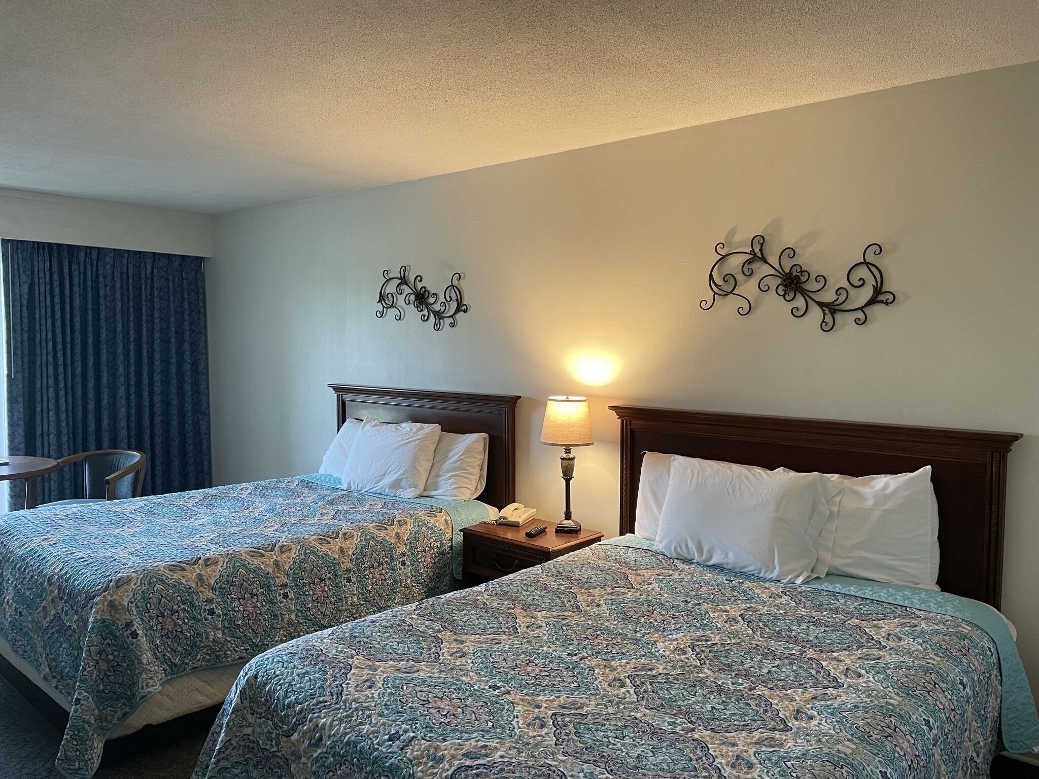 A hotel room with two beds, a nightstand with a lamp, and decorative wall art.