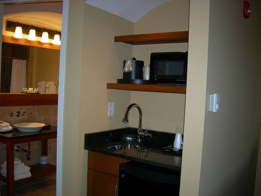 A compact kitchen with a sink, a microwave, and a shelf above the counter.