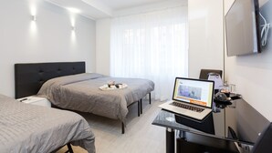 A modern hotel room with two beds, a desk with a laptop, a flat-screen TV, and a large window with sheer curtains. - Domus Arena (Rome)