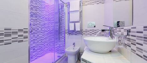 A modern bathroom with a glass-enclosed shower, a white sink, and a bidet.