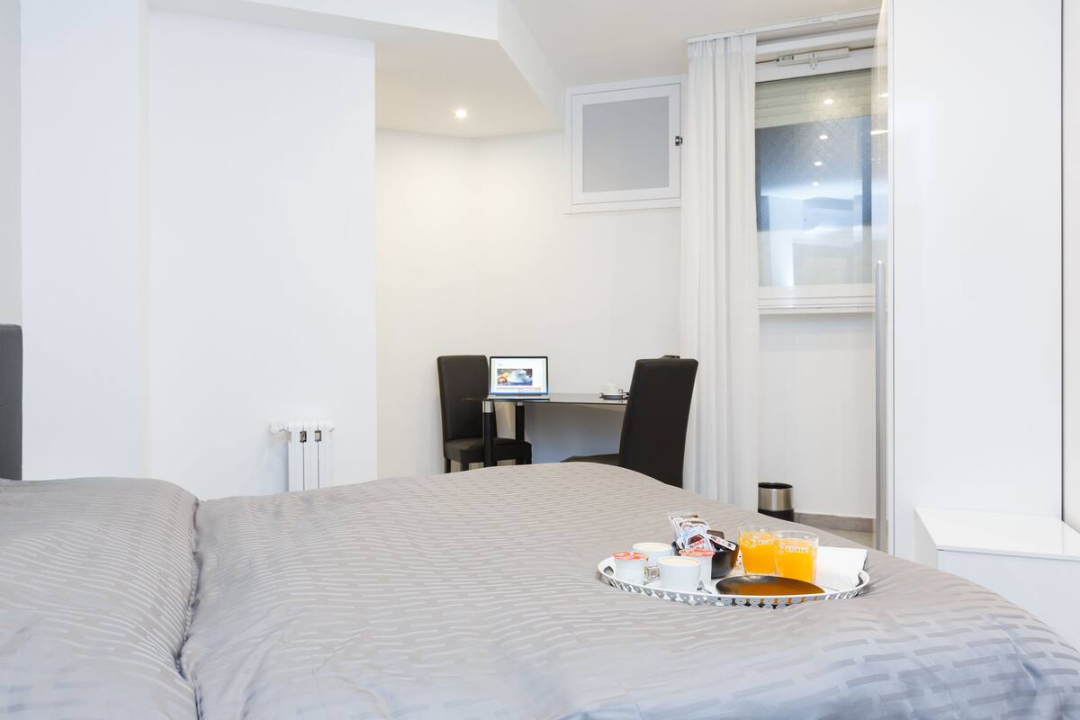 A hotel room with a bed, a desk with a computer, and a tray with breakfast items.