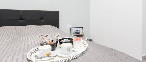 A neatly made breakfast tray with coffee cups, a bowl, and a plate on a bed with a grey headboard.