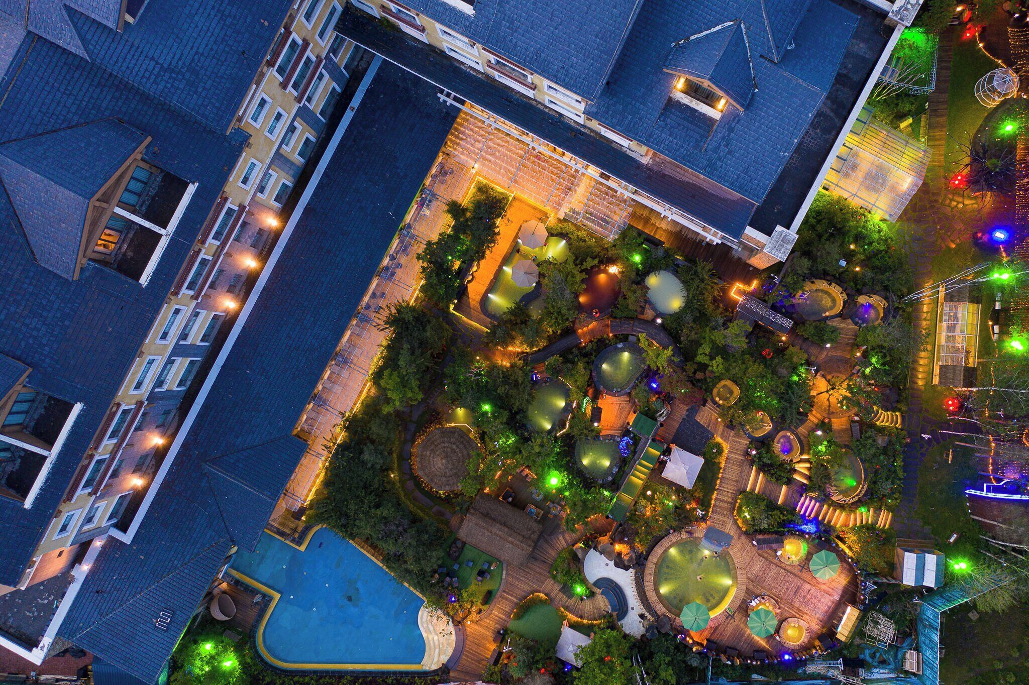 Vista aérea de un patio de hotel con piscina, múltiples zonas de estar y variada iluminación exterior.