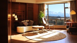 Ein stilvolles Wohnzimmer mit einer Couch, einem Sessel und einem runden Couchtisch. Ein großes Fenster bietet Blick auf die Berge.