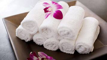 A set of neatly rolled white towels on a square tray with a purple orchid.