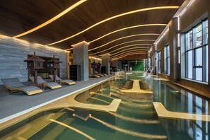 A modern indoor swimming pool with a curved design, lounge chairs, and a wooden ceiling with linear lighting. - Crowne Plaza Resort Changbaishan Hot Spring by IHG (Yanbian)