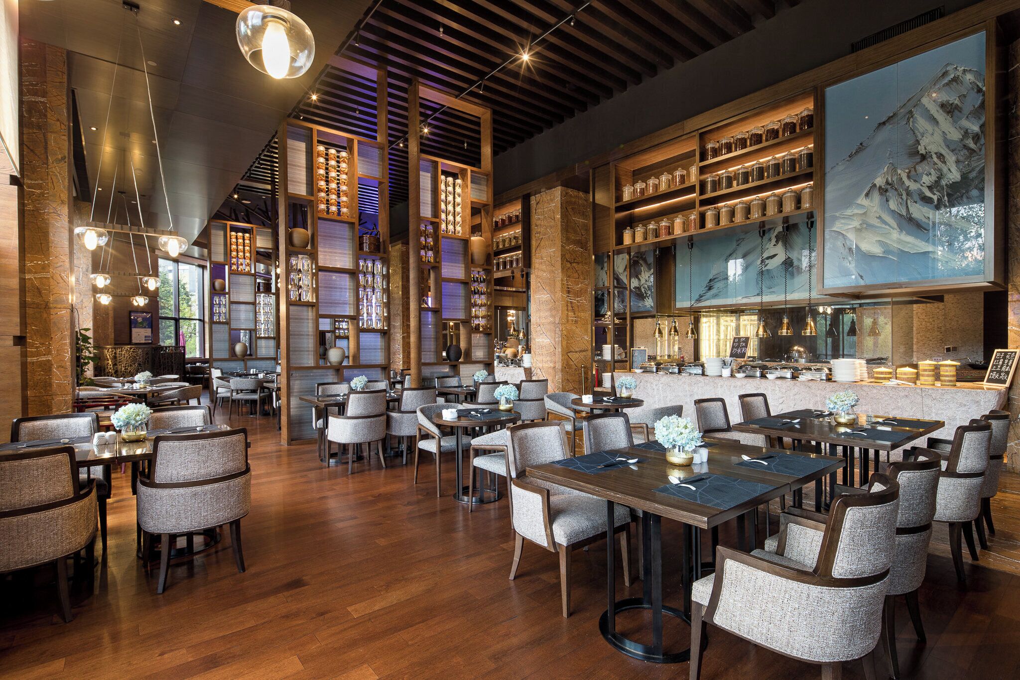Un restaurant doté de nombreuses tables et chaises, de poutres en bois au plafond et d’étagères remplies de bocaux.