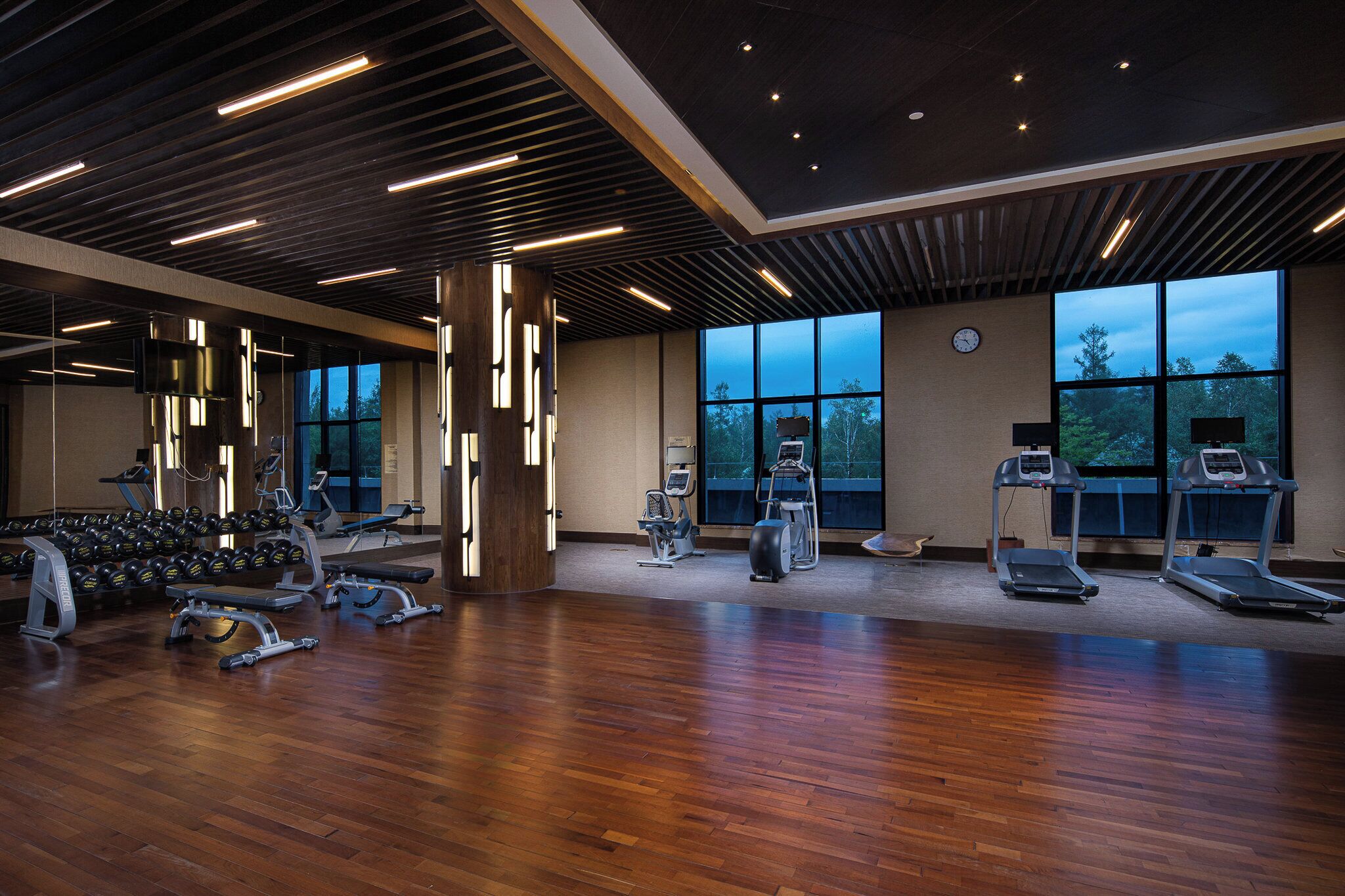 Ein Fitnessstudio mit unterschiedlichen Trainingsgeräten, großen Fenstern und Holzboden.