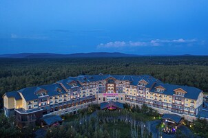 Un hotel grande de varios pisos con techo curvo, rodeado de un paisaje boscoso.