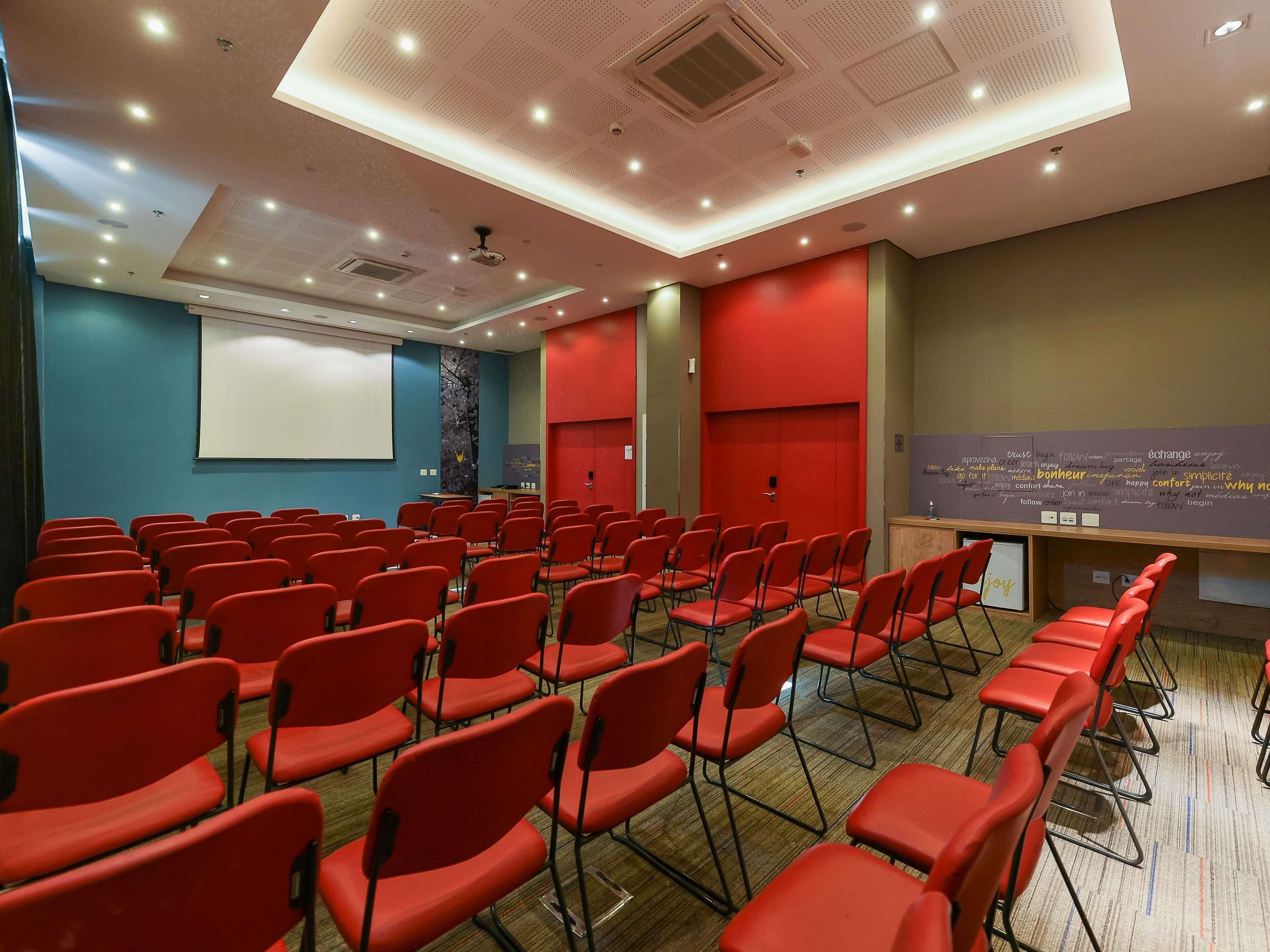 A conference room with rows of red chairs, a projector screen, and a whiteboard with motivational words.