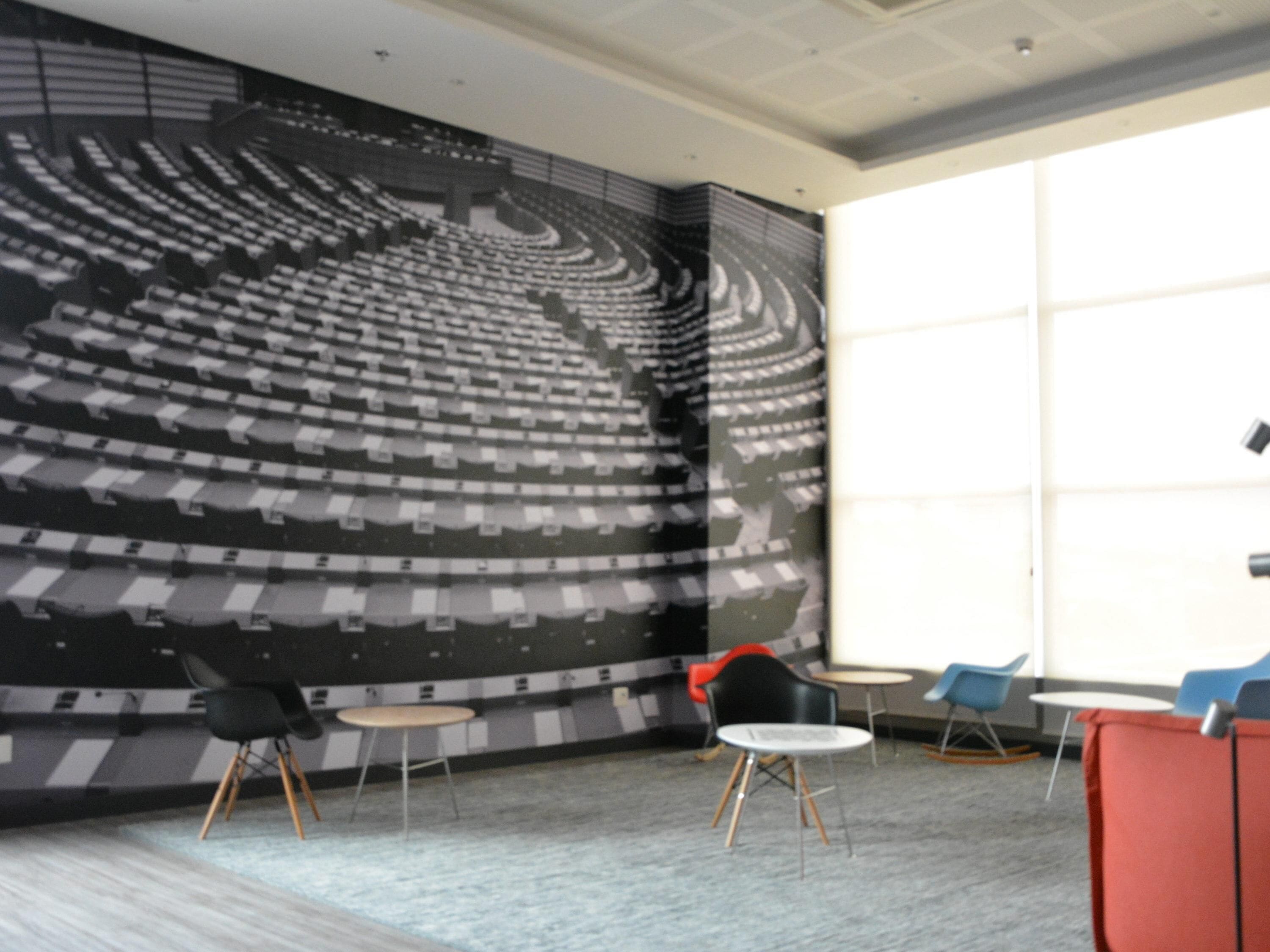 A modern interior with a large mural of an auditorium, a seating area with tables and chairs, and a large window providing natural light.