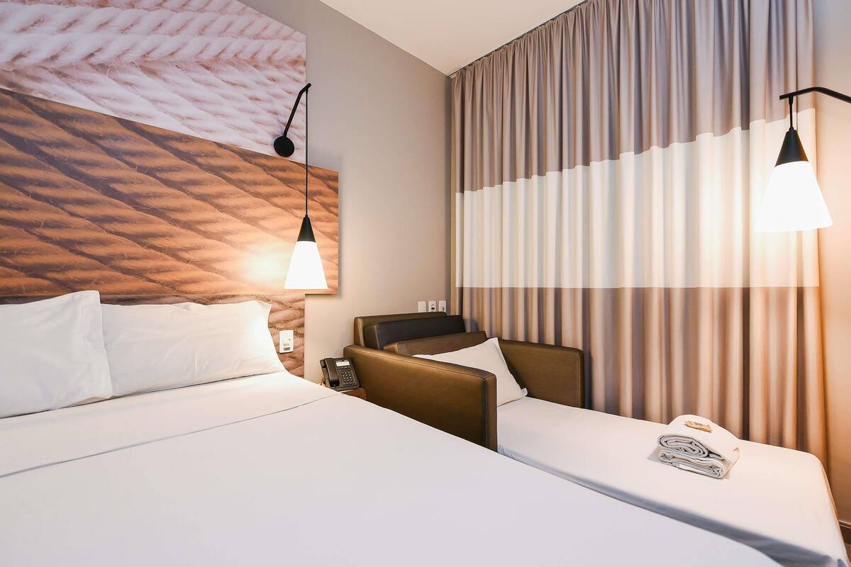 Une chambre d’hôtel avec un lit, un bureau, un téléphone et une fenêtre avec des rideaux.