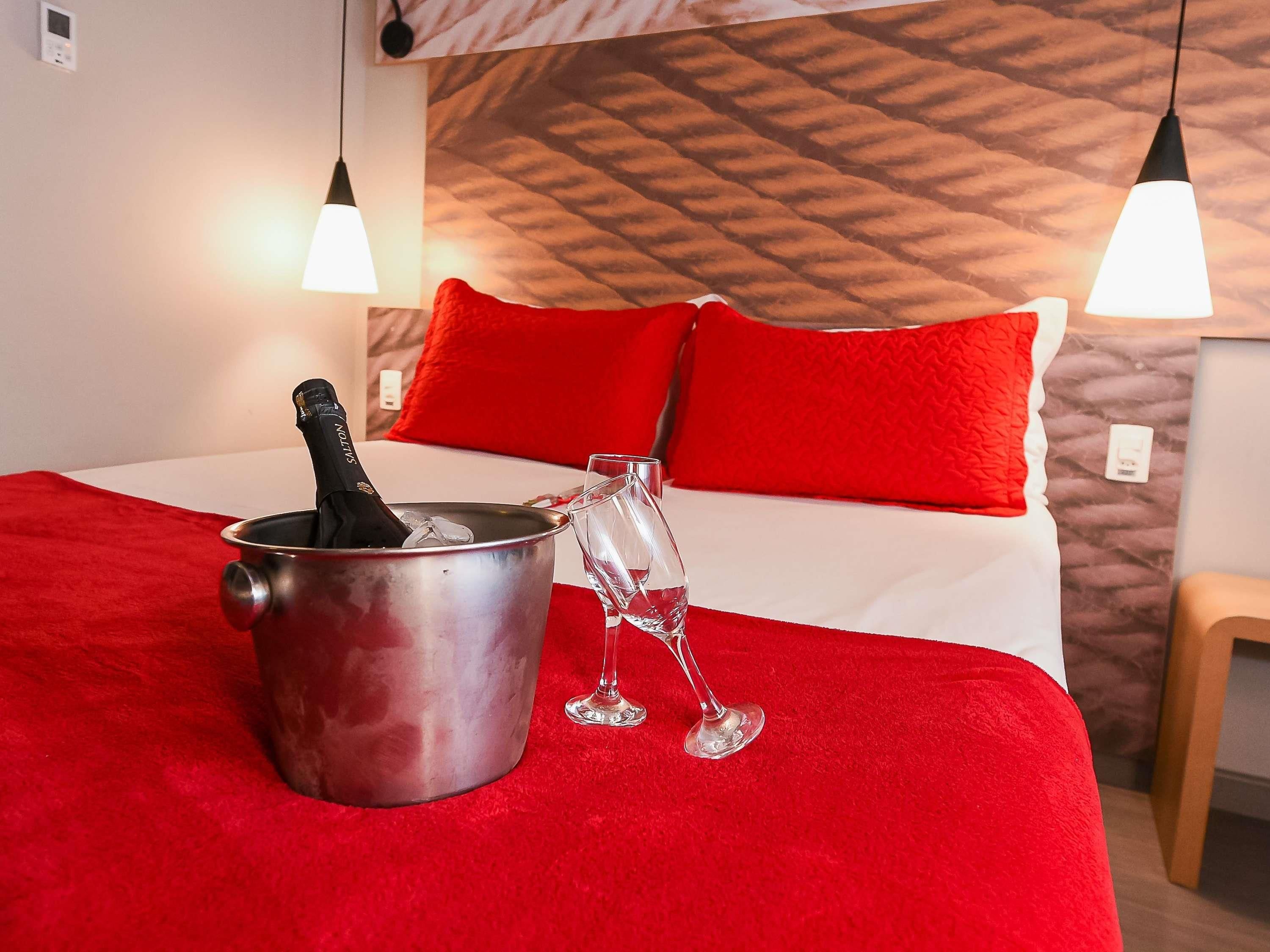 Uma cama com roupa de cama vermelha, um balde de champanhe e uma taça de vinho sobre um tapete vermelho.