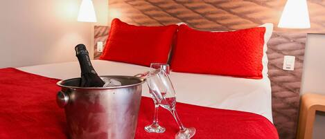 Uma cama com roupa de cama vermelha, um balde de champanhe e uma taça de vinho sobre um tapete vermelho.