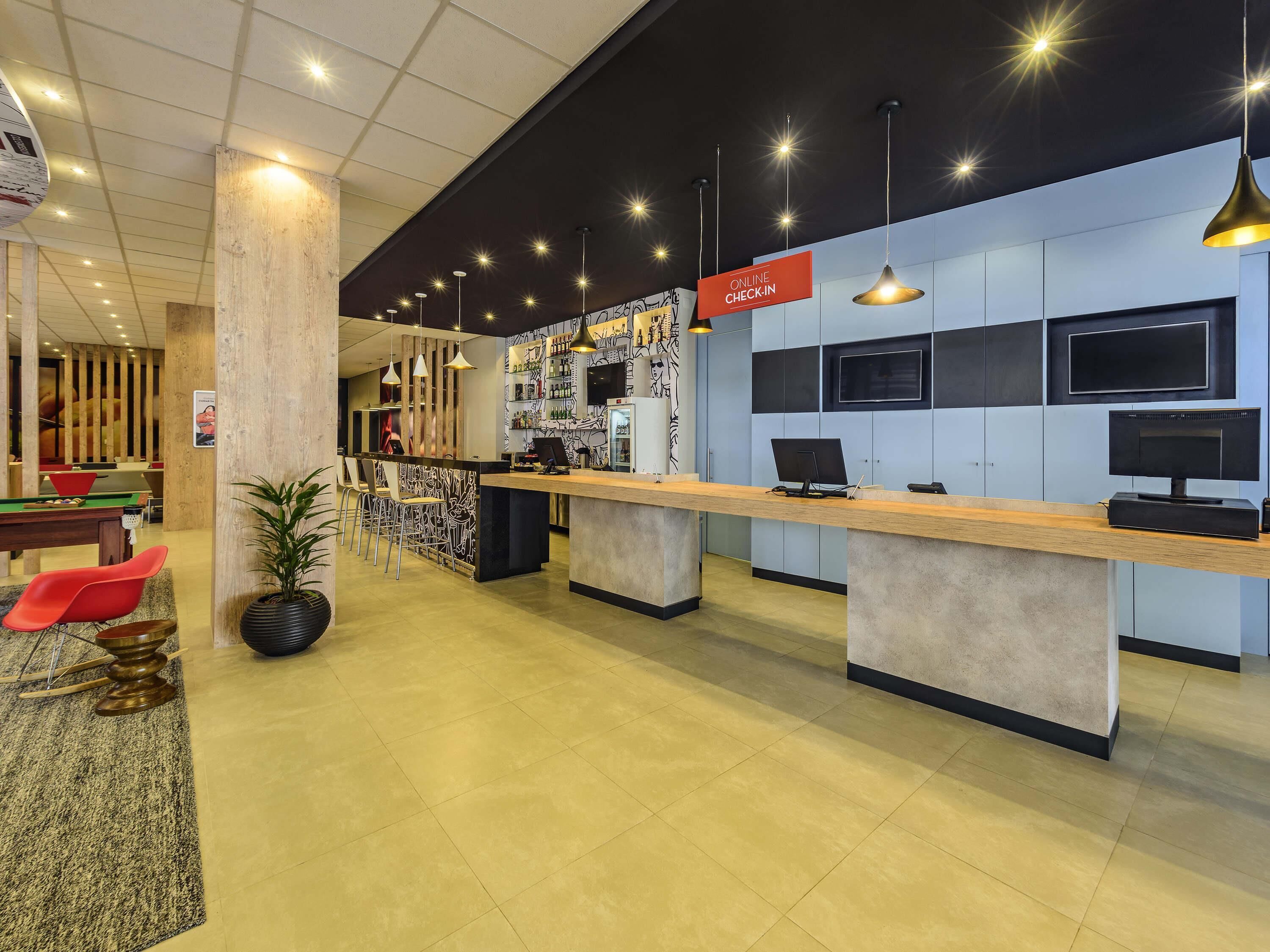 A modern hotel lobby with a reception desk, seating area, and a bar.
