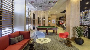A modern lounge area with a pool table, red sofa, and a bar area with a mural. - ibis Jacarei (Jacarei)