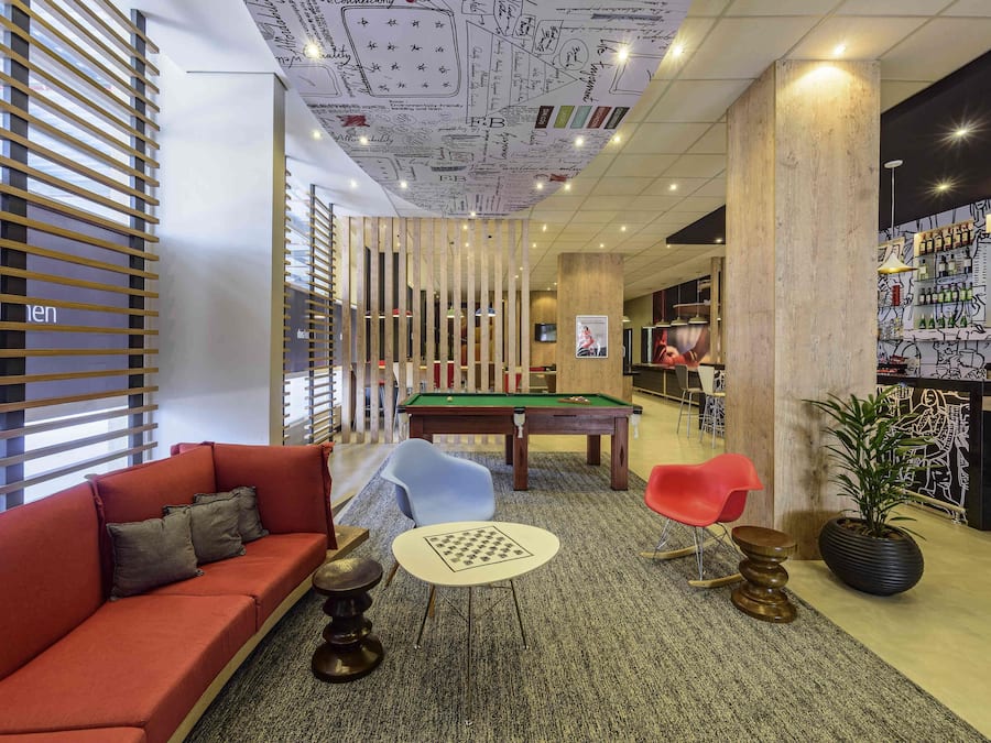A lounge area with a pool table, a red sofa, a small round table, and a bar area with bottles.
