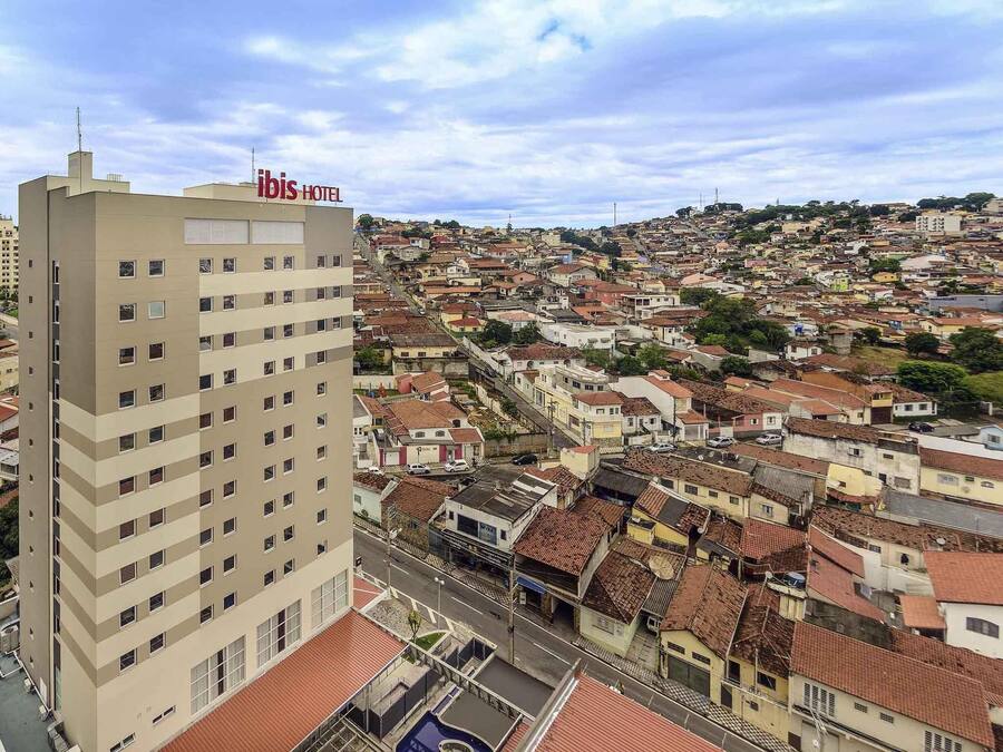 A hotel with multiple floors, a rooftop pool, and a view of a densely packed urban area with terracotta-roofed buildings.