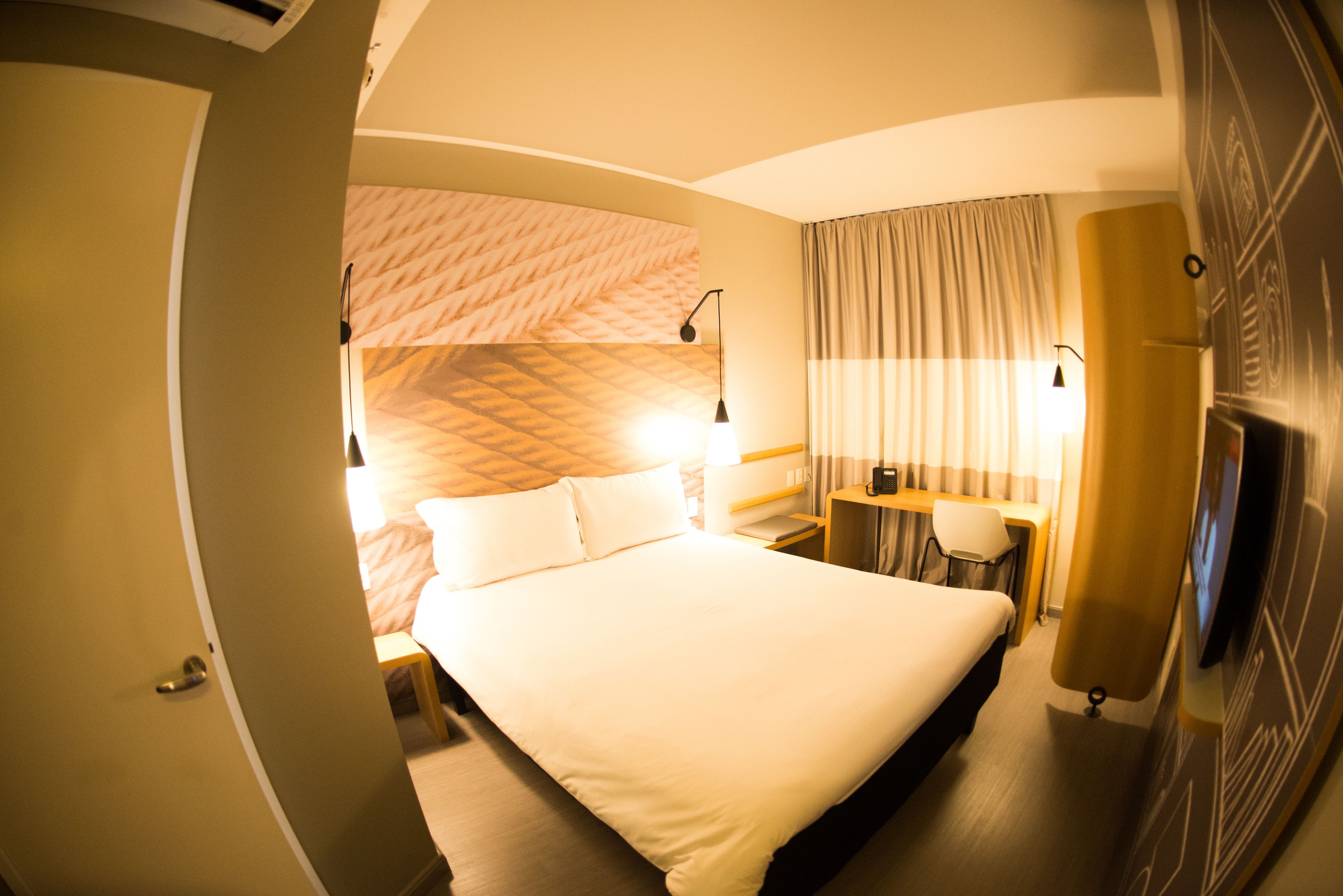 Ein Hotelzimmer mit einem großen Bett, einem Schreibtisch, einem Sessel, einem Fernseher und einer Wand mit Muster.