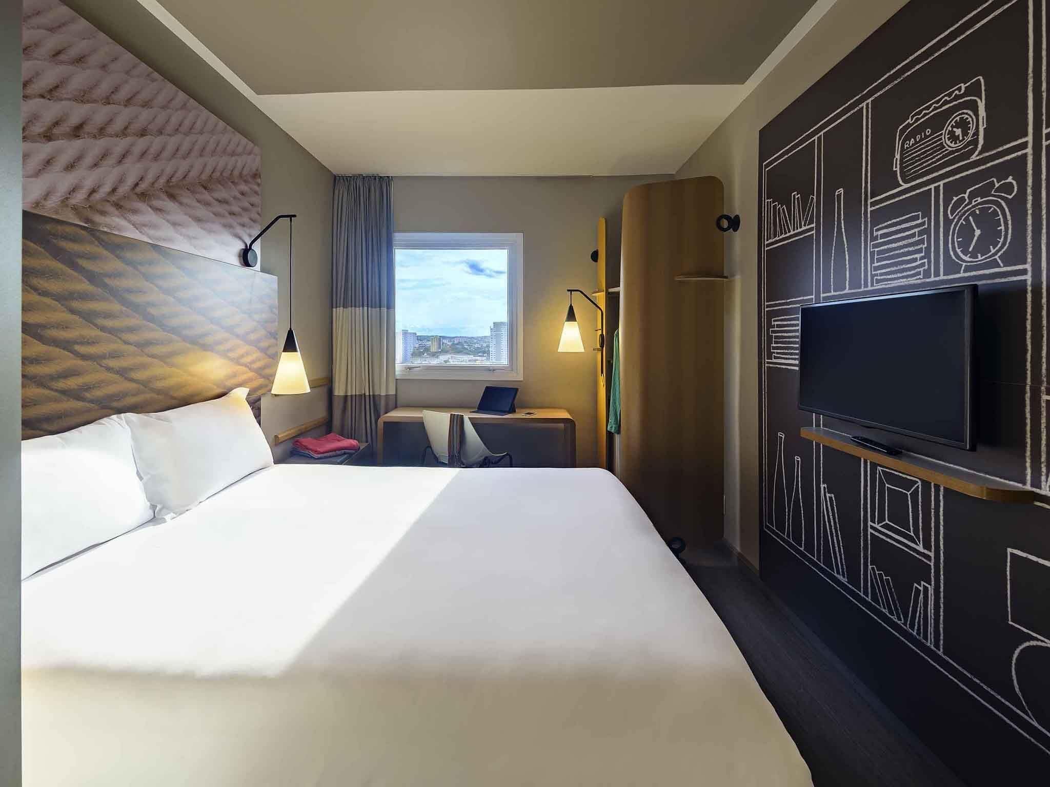 Hotelkamer met een groot bed, een televisie, een bureau met een laptop, een raam met uitzicht en een muur met een schoolbord ontwerp.