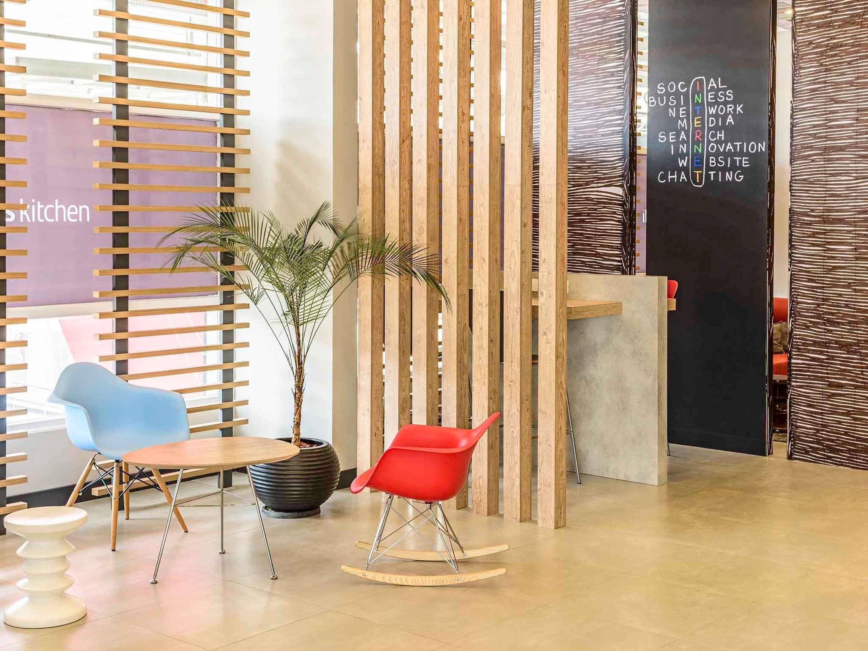 Un interior moderno con un panel divisor de madera con listones, una planta en maceta, dos sillas y una pizarra con palabras relacionadas con negocios.
