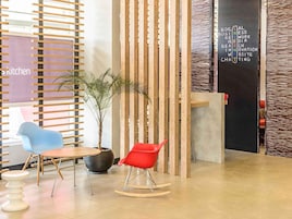 Un interior moderno con un panel divisor de madera con listones, una planta en maceta, dos sillas y una pizarra con palabras relacionadas con negocios.