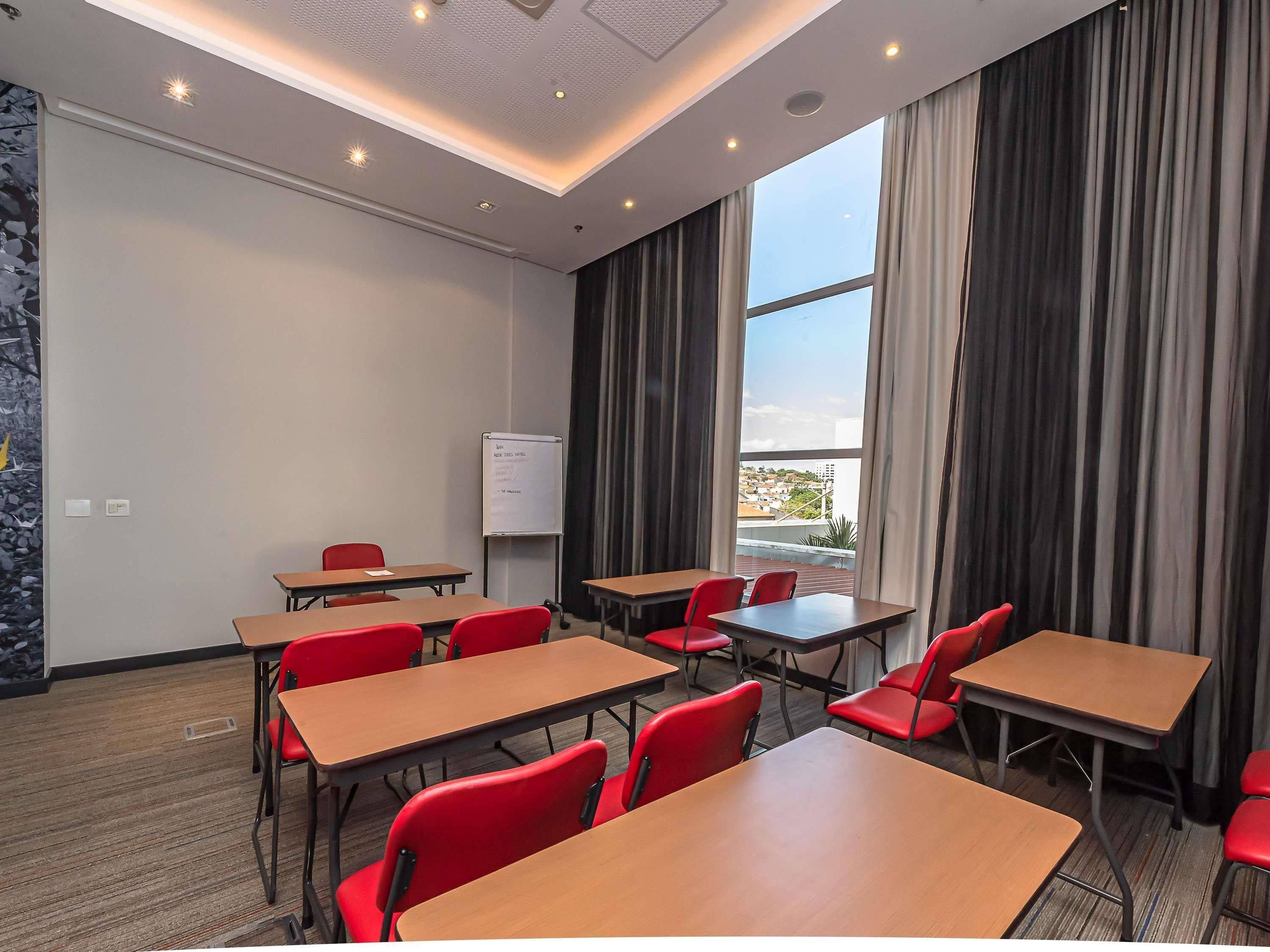 Un salón de conferencias con mesas y sillas, una pizarra blanca y vistas amplias a través de ventanas grandes.