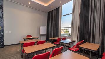 Un salón de conferencias con mesas y sillas, una pizarra blanca y vistas amplias a través de ventanas grandes.