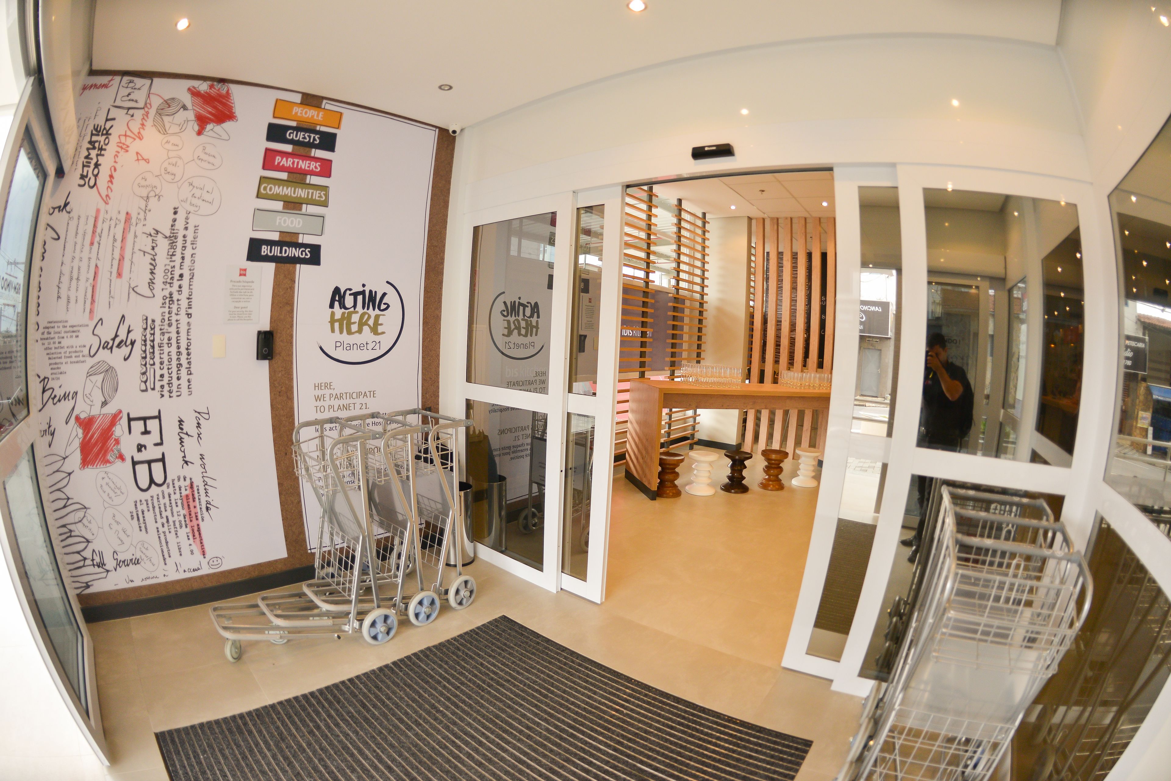 Um interior moderno com uma parede curva exibindo diversos avisos e um letreiro com a inscrição 'Acting Here Planet 21'.