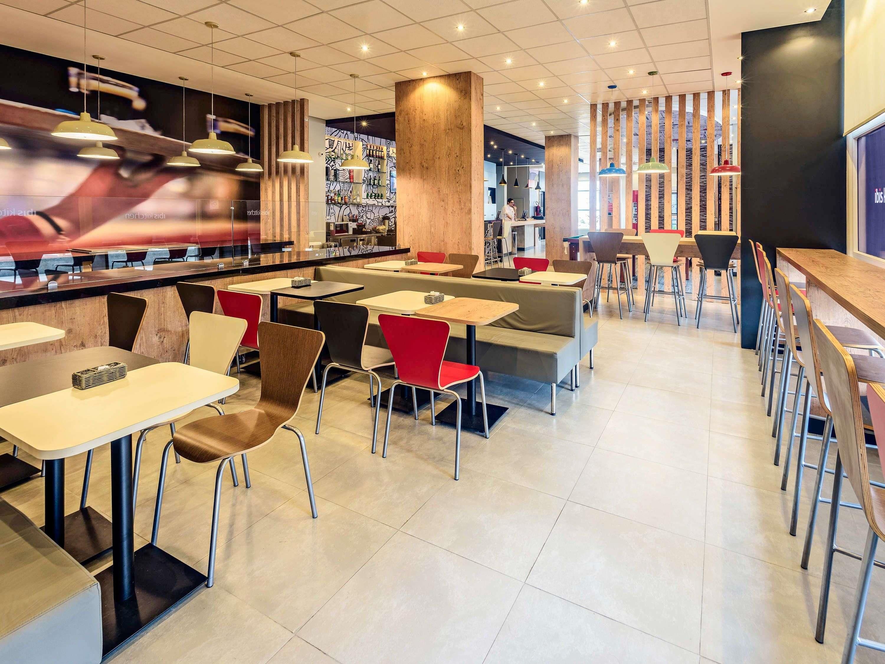 A modern restaurant interior with multiple seating options including tables and booths, a bar area, and a visible kitchen in the background.
