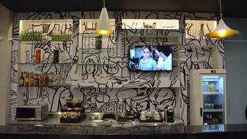 Zona de bar con televisor, estantes con botellas, microondas y refrigerador.