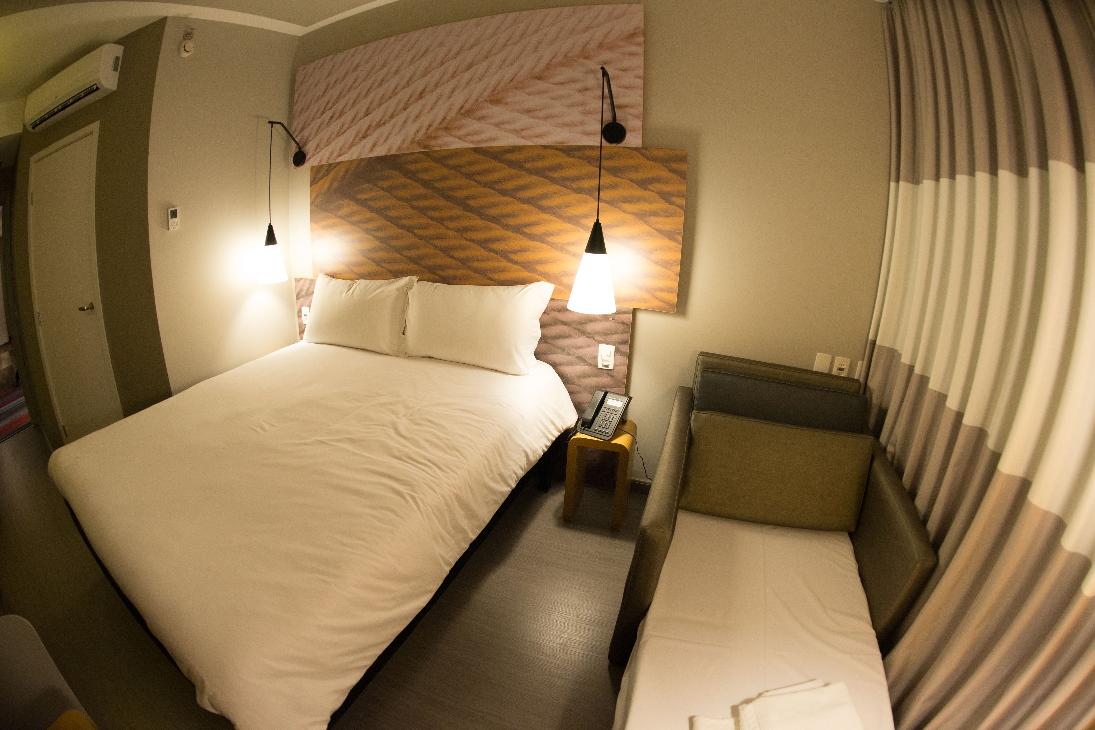 A hotel room with a large bed, a smaller bed, a bedside table with a phone, and a wall-mounted light fixture.