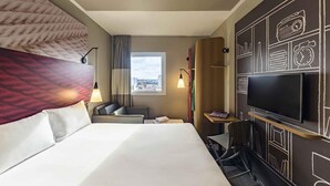 A hotel room with a large bed, a TV, a window with a city view, and a wall with chalkboard-style drawings. - ibis Jacarei (Jacarei)