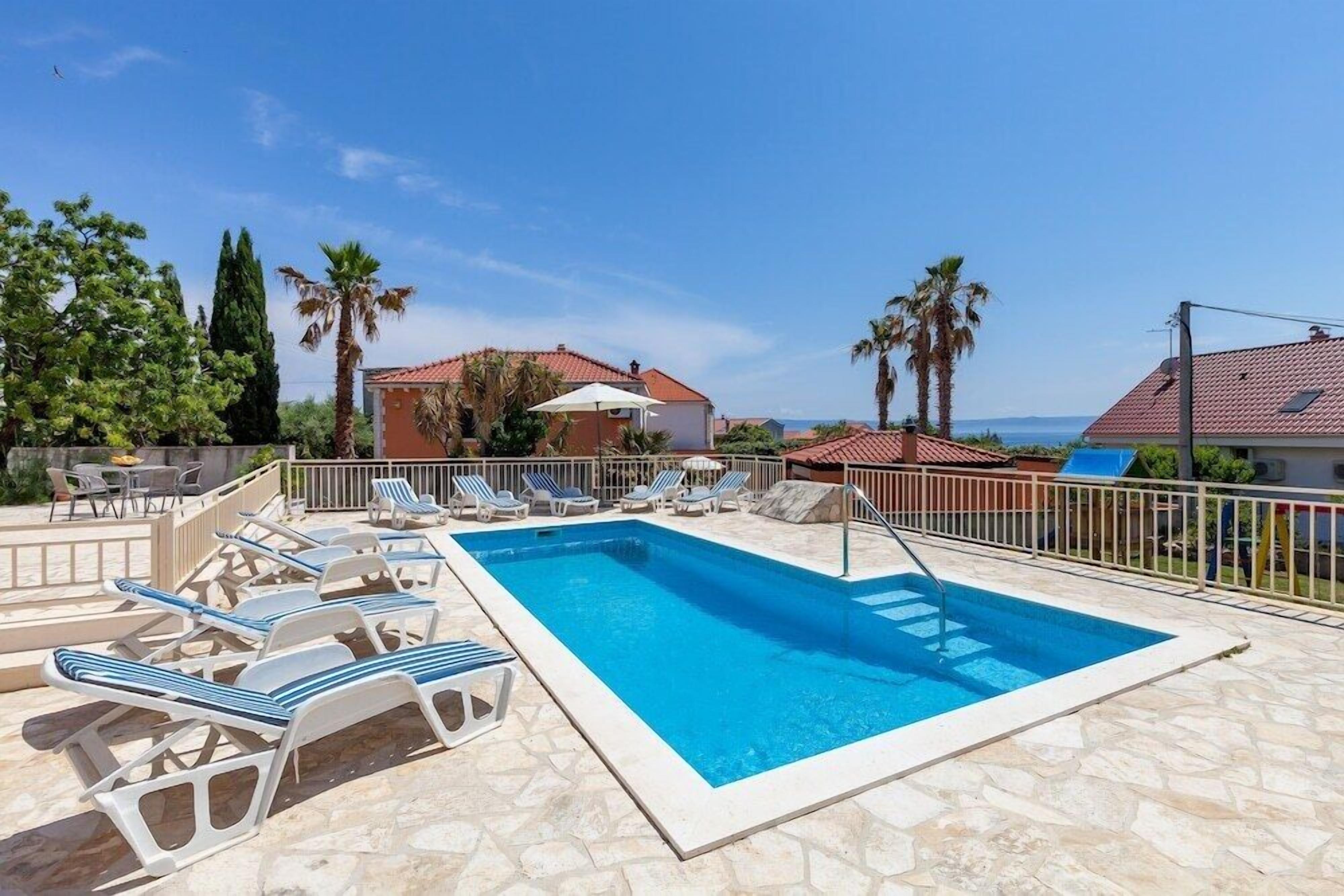 Piscina rectangular con borde de piedra, rodeada de sillas de descanso y una barandilla.