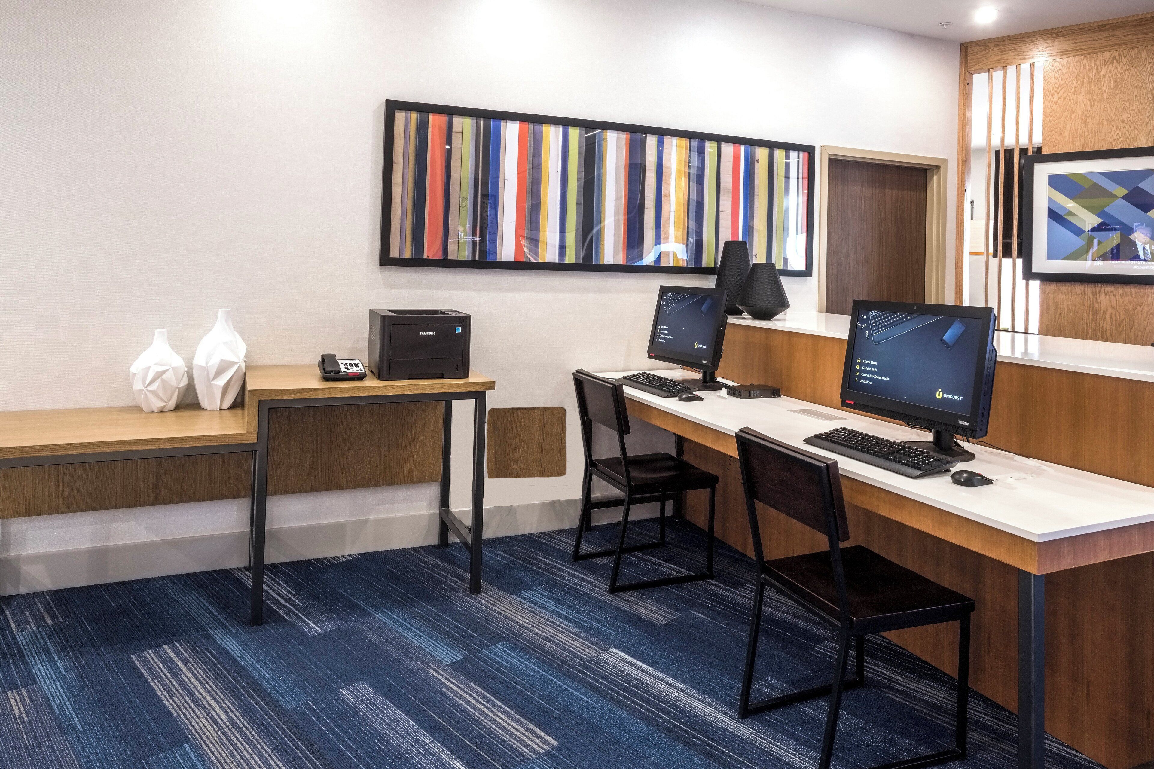 En hotellobby med en receptionsdisk, två datorskärmar, en telefon och inramade konstverk på väggen.