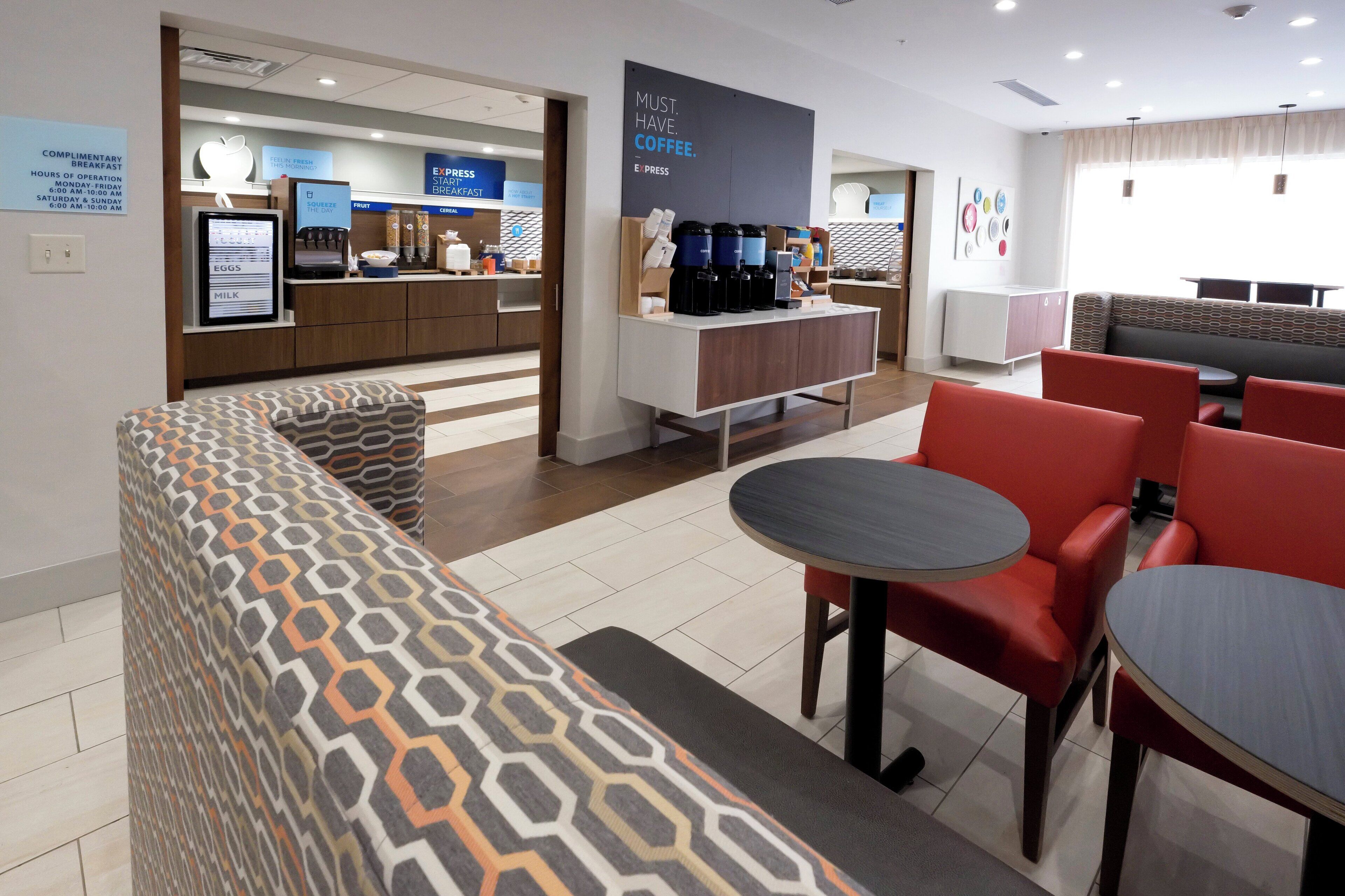 En moderne hotellobby med kaffestation, siddeområde og en disk med morgenmadstilbud.