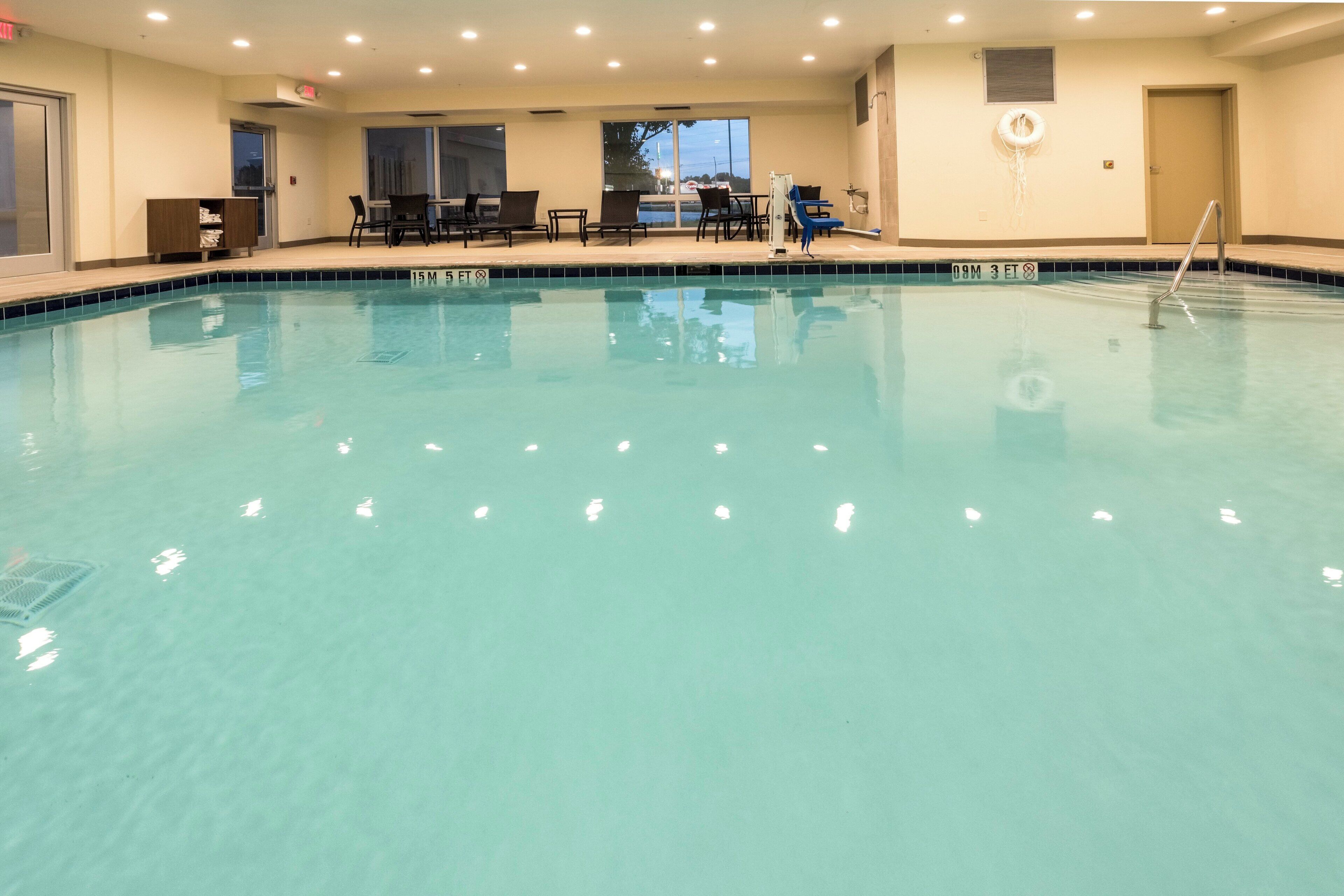 A swimming pool with lounge chairs and a table, surrounded by walls with windows.