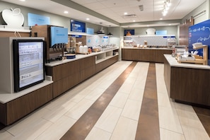Un moderno comedor con un menú digital, una estación de bebidas de autoservicio y diversas opciones de comida.