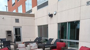 An outdoor seating area with wicker furniture and red cushions, a building with large windows, and a sign for 'Hotel Express Suites'. - Holiday Inn Express & Suites Commerce by IHG (Commerce)