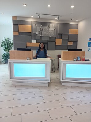 A reception desk with a modern design, a potted plant, and a sign indicating a Holiday Inn Express.