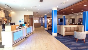 A hotel reception area with a modern design, featuring a reception desk, seating area, and a view of the dining space. - Holiday Inn Express & Suites Commerce by IHG (Commerce)