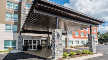 A modern building with a covered entrance, stone pillars, and a parking lot.