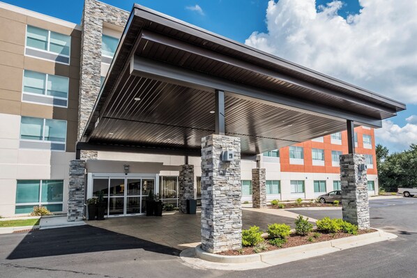 A modern building with a covered entrance, stone pillars, and a parking lot.